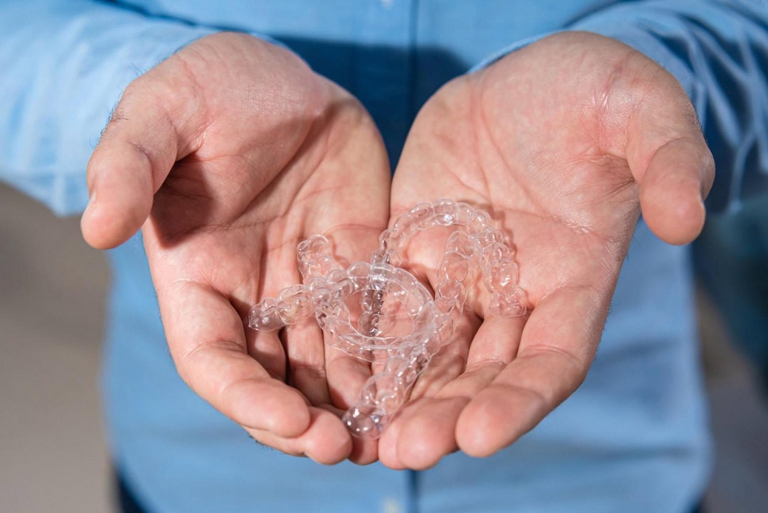Hands holding a set of transparent clear aligners for teeth straightening